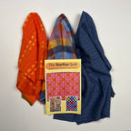 Three folded quilts in different patterns and colors (orange floral, blue polka dots, and multicolor plaid) are arranged on a white background with a quilt pattern booklet titled 'The Surprise Quilt' placed on top.