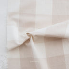 A close-up of a soft fabric with a pale blush pink and off-white gingham check pattern, draped to show its texture and weave.